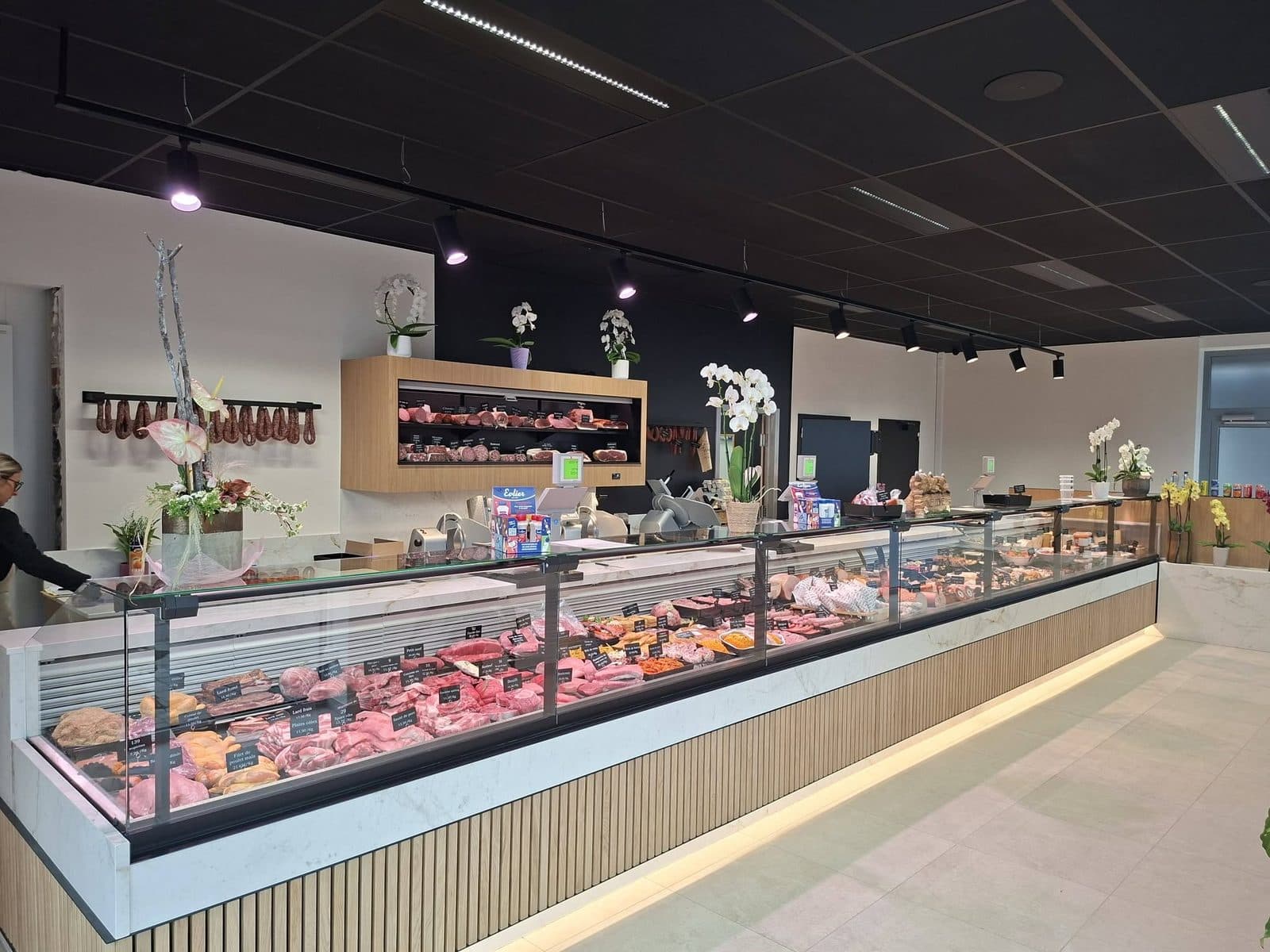 Le comptoir de la boutique : la longue vitrine réfrigérée, la charcuterie suspendue au mur et le présentoir en bois